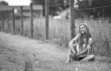 Smiling woman sitting barefoot near a fence.