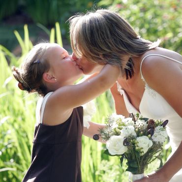A woman and a girl share a kiss outdoors.