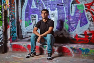 Young man sitting in front of colorful graffiti wall.
