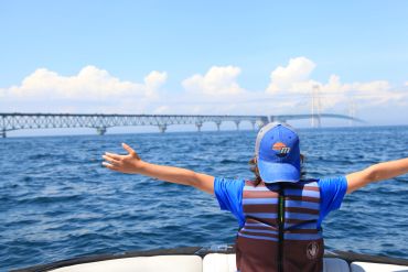 Person enjoying a boat ride with open arms and a bridge in the background.
