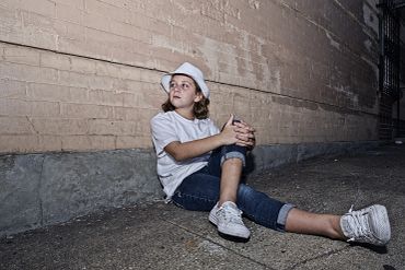Girl sitting on the ground against a brick wall.