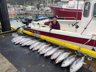 a man on a boat with tuna lined up on dock 