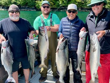 group of salmon fisherman holding up their catch on boat