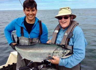 two men hold up chinook salmon on boat