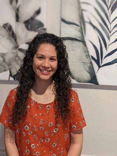 Young woman with curly hair smiles wearing an orange floral blouse.