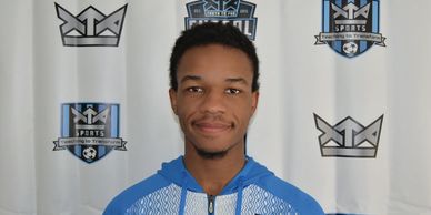 Young man in a blue sports jacket smiles in front of a sports-themed backdrop.