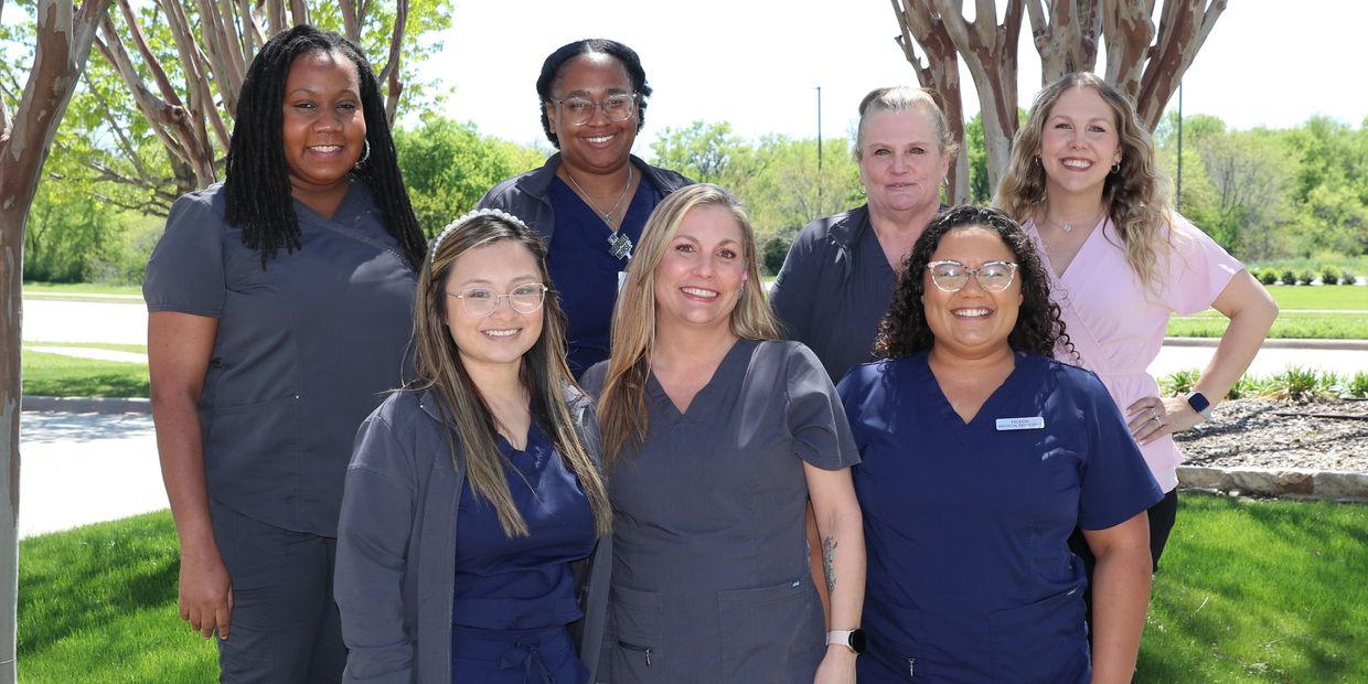 Group of smiling women in scrubs outdoors.