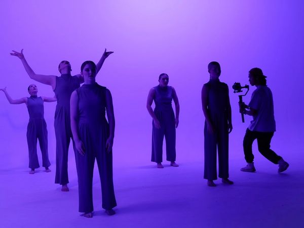 Dancers in purple lighting with a cameraman filming them.