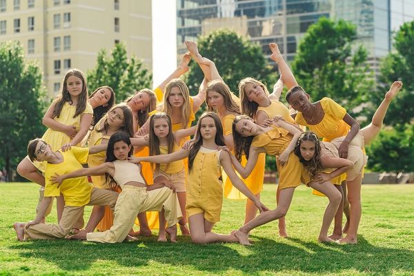 Group of children in yellow performing a creative outdoor dance pose.