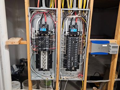 Two electrical breaker panels installed in a wooden frame in a basement.