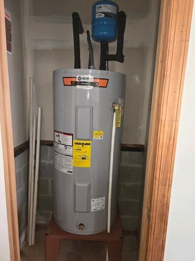 A gray water heater installed on a red stand in a small utility closet.