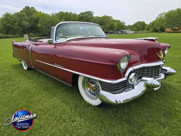 Classic maroon convertible car parked on green grass under a cloudy sky.