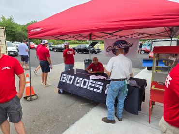Outdoor event with a table labeled 'BID GOES' under a red canopy.
