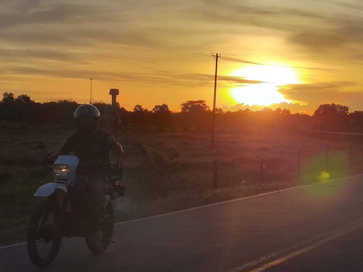 Motorcycle rider on a road during a vibrant sunset.