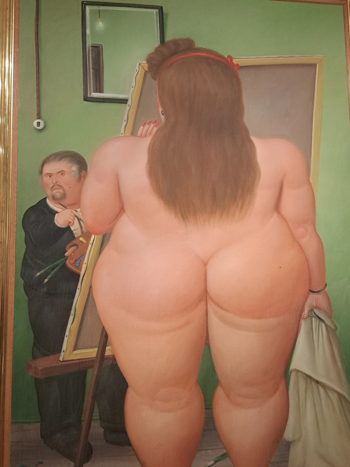 A painter captures the back of a nude woman standing in front of a mirror.