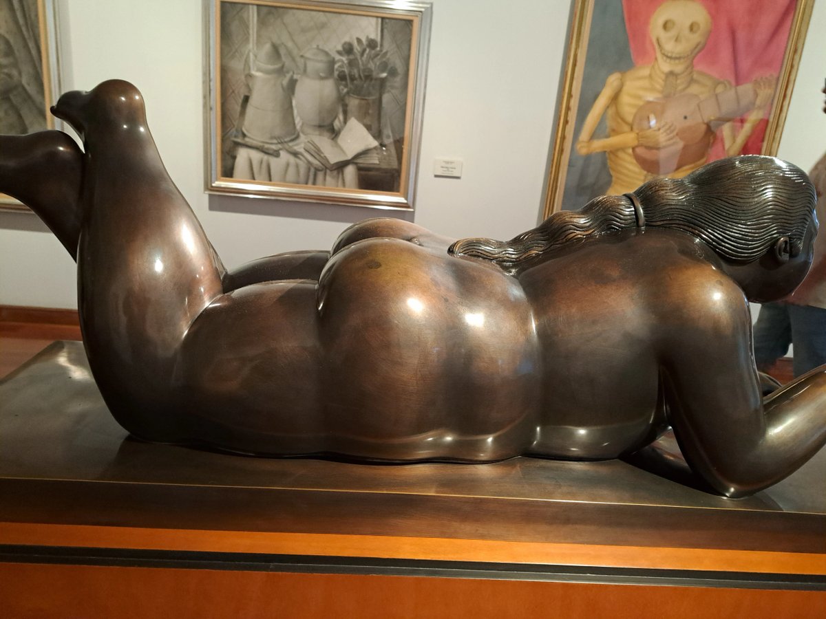 Bronze sculpture of a reclining, voluptuous woman with wavy hair in an art gallery.