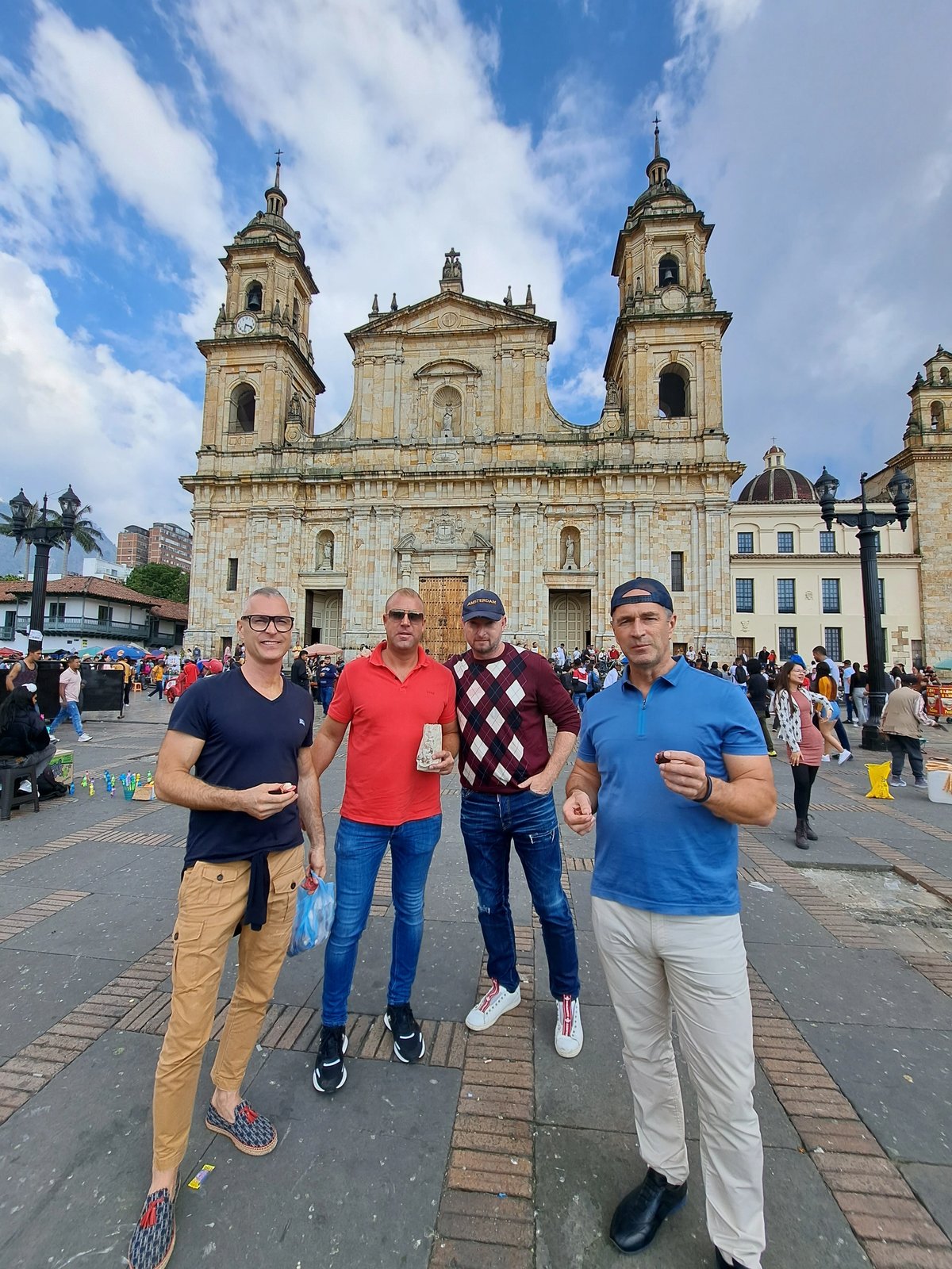 Four men posing in front of a historic cathedral on a busy day.