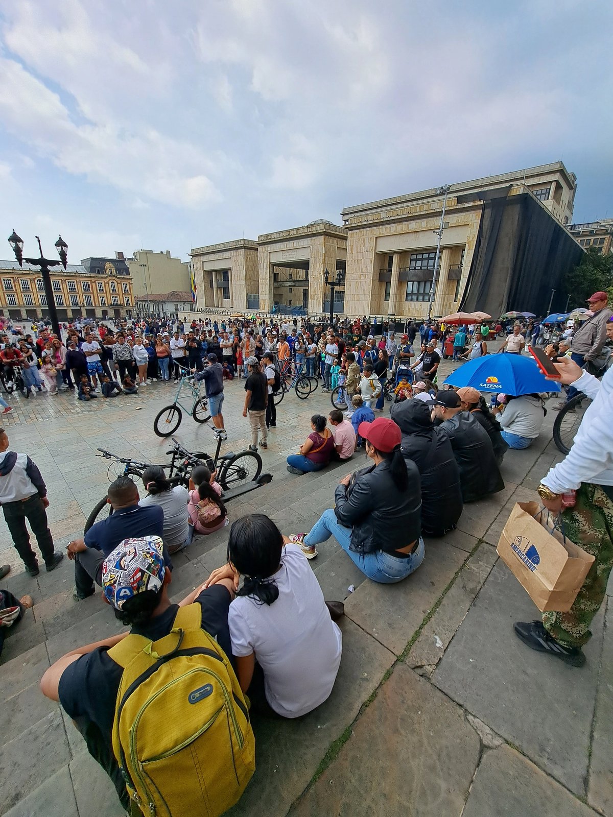 Crowd watching street performers with bicycles in a historic plaza.