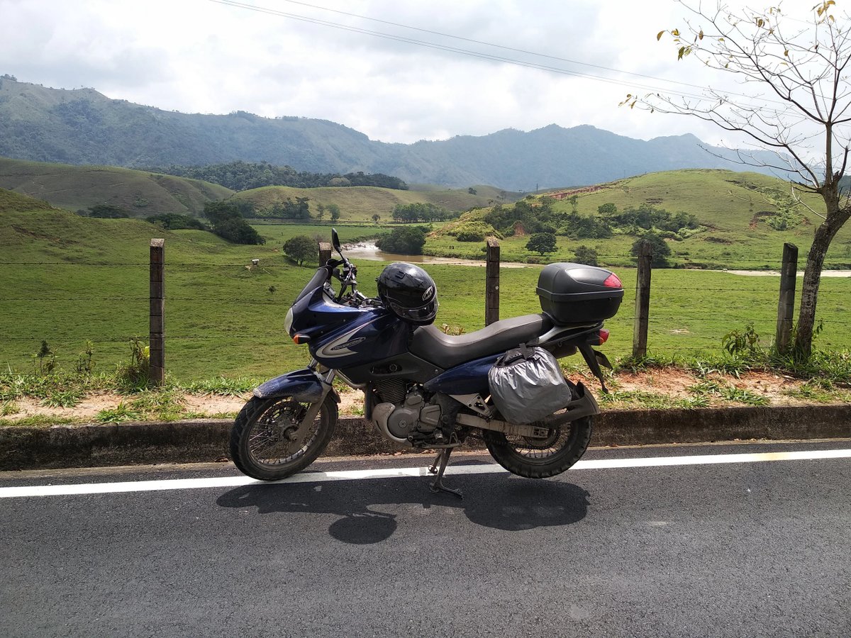 A motorcycle parked on the road with green hills and mountains in the background.