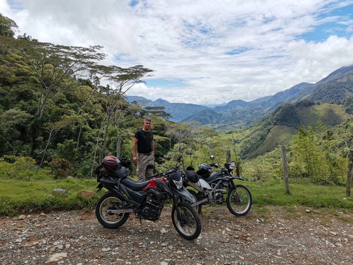 Man standing next to motorcycles with scenic mountain view.
