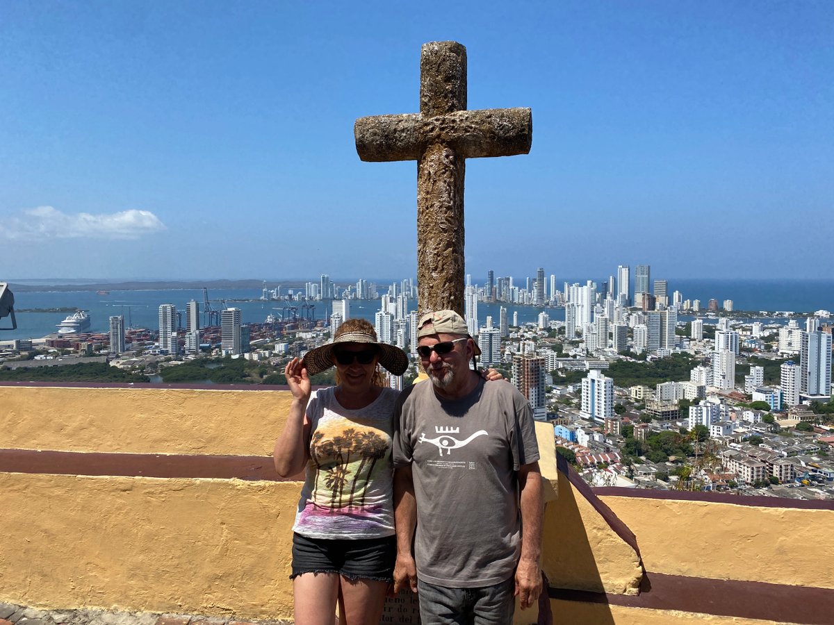 Couple posing in front of a large stone cross overlooking a coastal city skyline.
