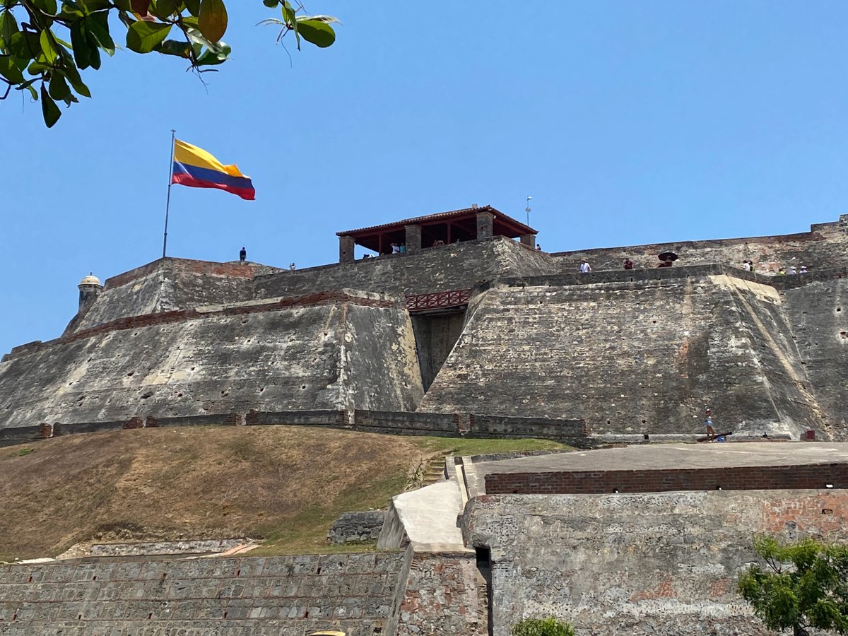 Historic stone fortress with Colombian flag atop under clear blue sky.