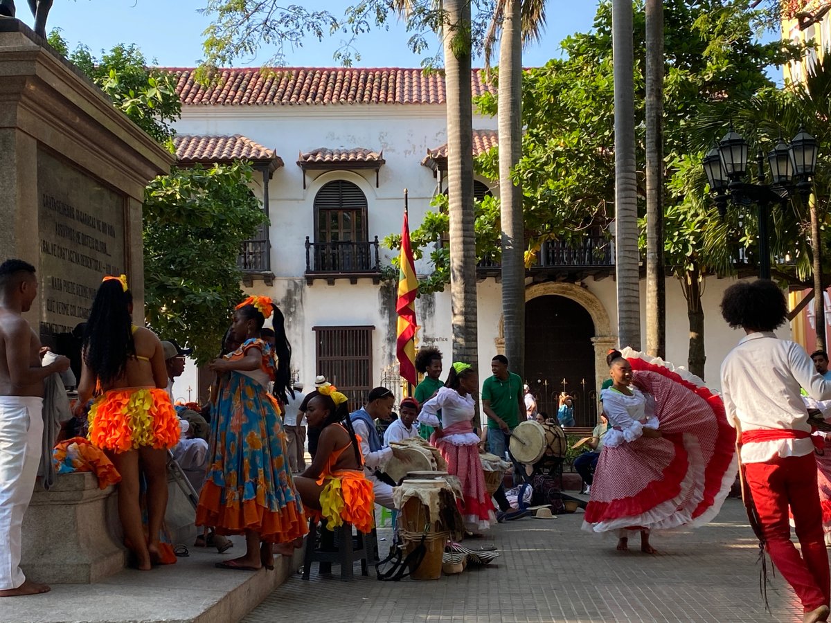 Colorful traditional dancers perform in a lively street scene with historic architecture.