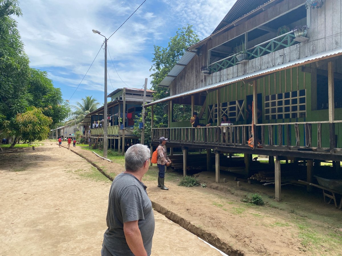 People walking and standing by stilt houses in a rural village under a blue sky.