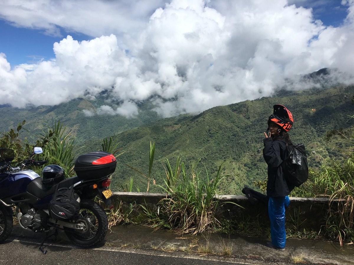 Person with helmet posing near motorcycles overlooking misty mountains.