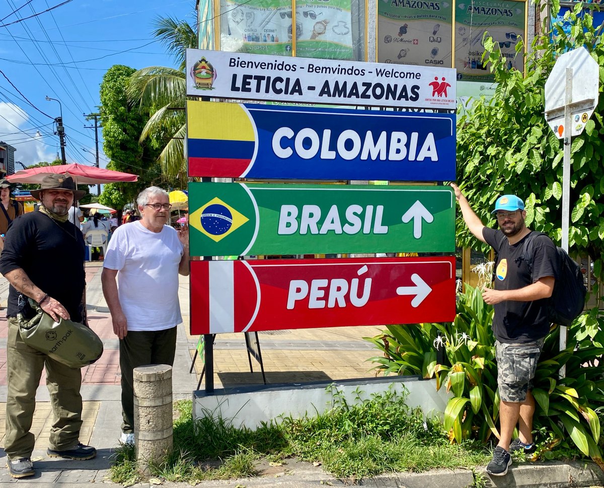 Three men posing near a sign pointing to Colombia, Brazil, and Peru in Leticia, Amazonas.