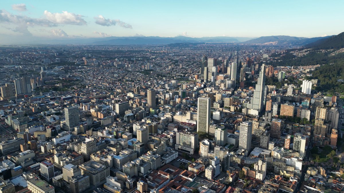 A sprawling cityscape with tall buildings and distant mountains under a clear sky.