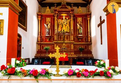 Altar adornado con flores y cruz dorada en iglesia.