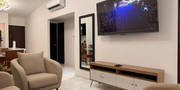 Cozy living room with beige armchairs, wall-mounted TV, and wooden cabinet.