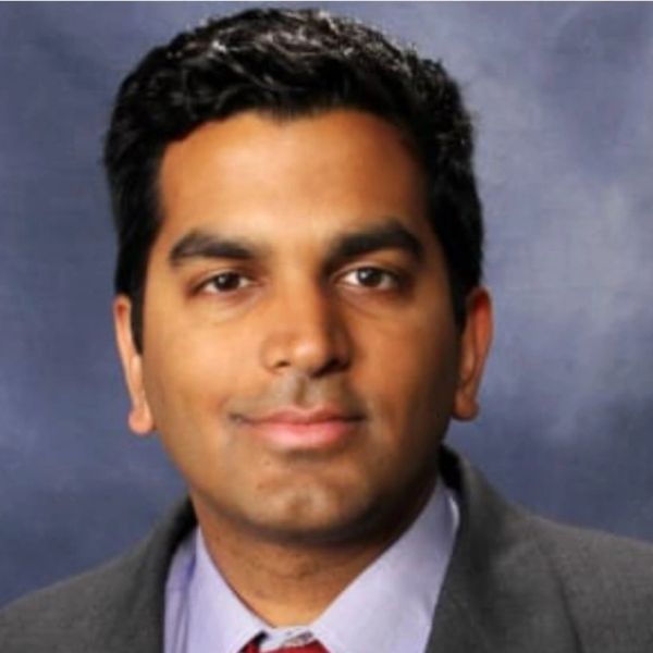 Professional headshot of a man in formal attire with a neutral background.