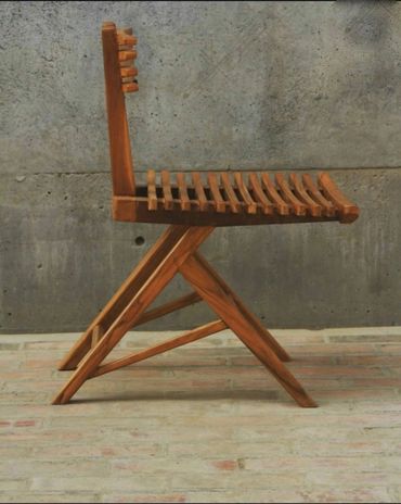 A wooden chair with a slatted seat and backrest against a concrete wall.