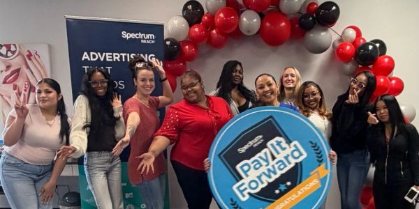 Group of smiling women posing with a Pay It Forward sign and balloons.