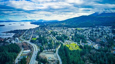 Aerial view of a coastal city with highways, greenery, and mountains in the background.