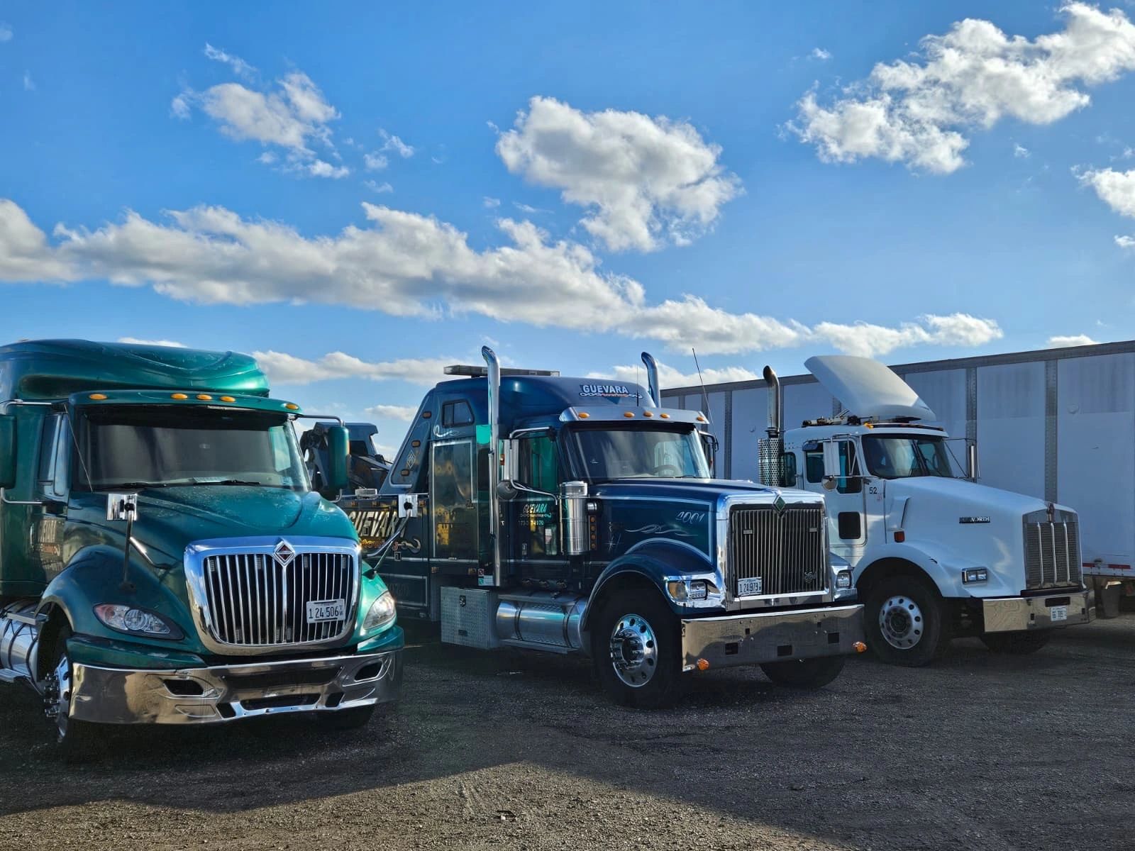 Three heavy-duty trucks parked under a blue sky with scattered clouds.