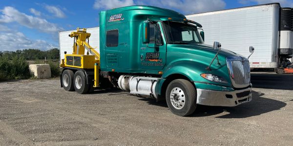 Green heavy-duty tow truck parked on a gravel lot under blue skies.