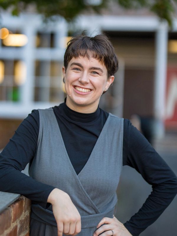 A white nonbinary person with blue eyes and short hair smiles at the camera.