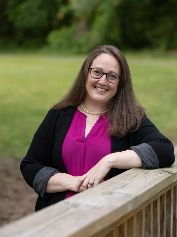 A smiling white woman leaning on a wooden bridge.
