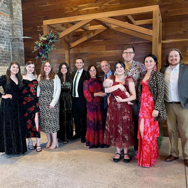A group photo of people dressed formally at an indoor event under a wooden arch. Family business