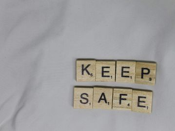 Scrabble tiles spelling out 'KEEP SAFE' on a gray fabric.