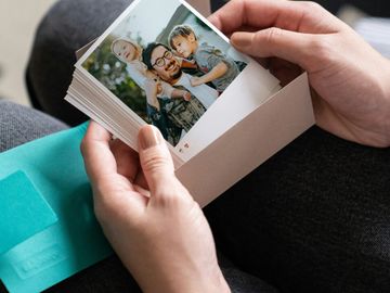 Hands holding a stack of photos of memories, and the top photo is of a smiling man with two children.