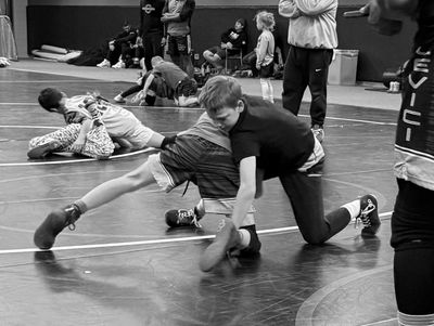 Two boys wrestling in a gym during a wrestling practice session.