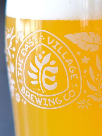 A glass of beer with The East Village Brewing Co logo.