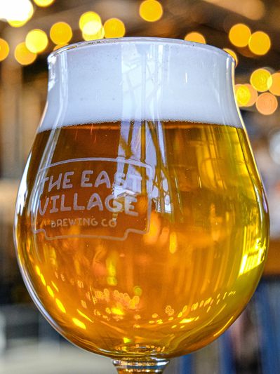 A tulip glass of golden beer with frothy head and brewery logo.