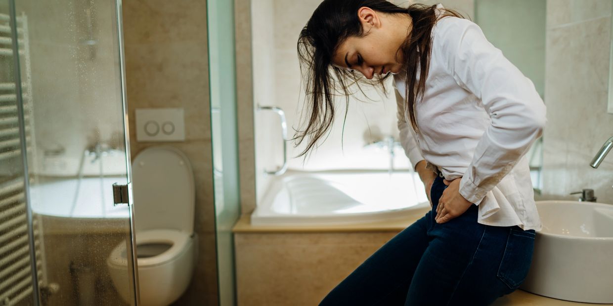 woman in bathroom holding pelvic area with look of pain on her face