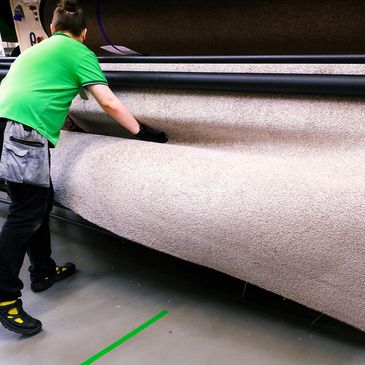person in a green shirt loading a very large section of carpet into a machine