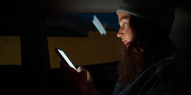 woman in back seat of a dimly lit car looking at her phone